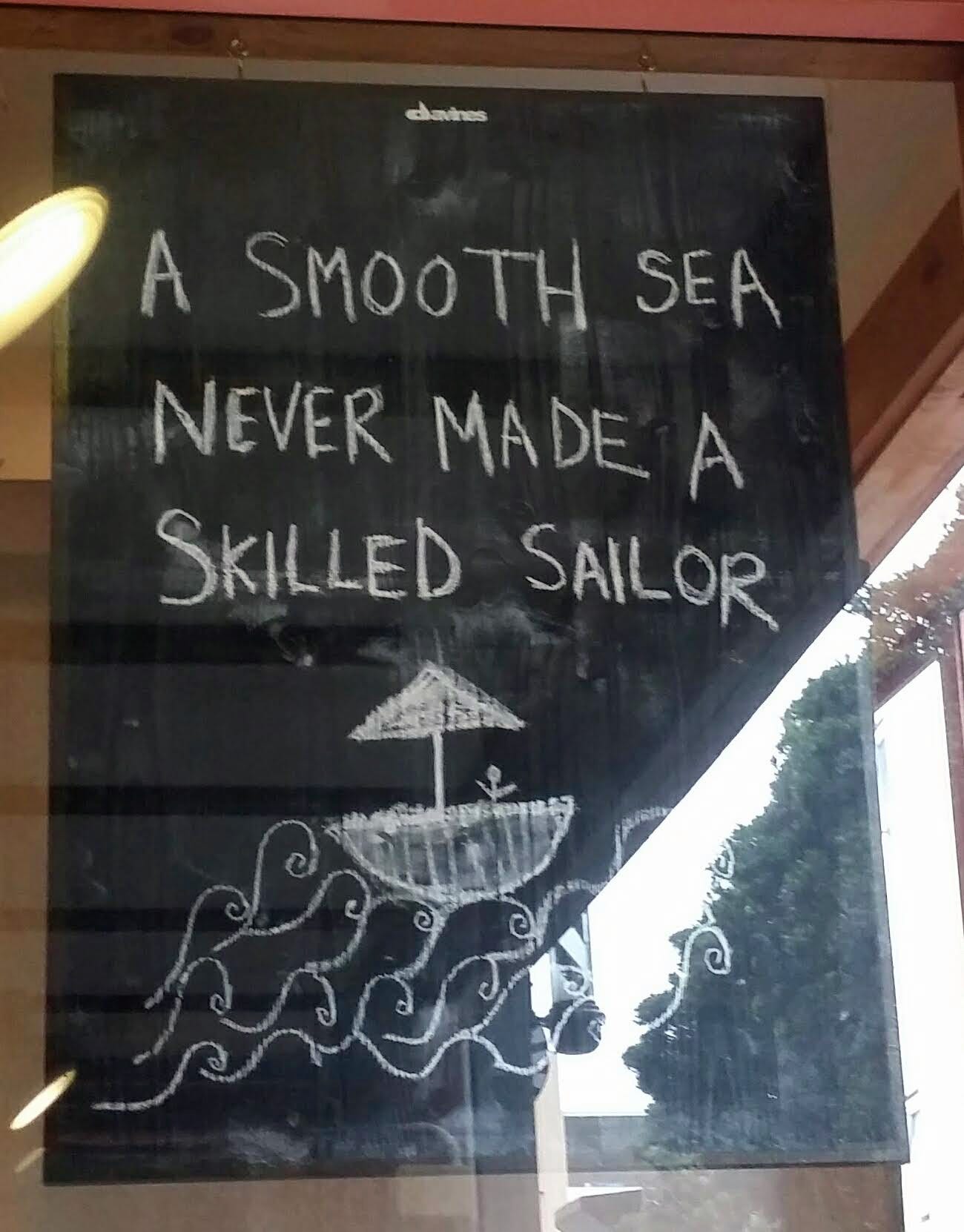 A chalkboard sign in a window reading "A smooth sea never made a skilled sailor"